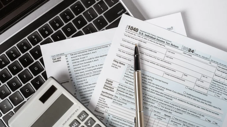Individual income tax planning with a 1040 tax return, calculator, and laptop arranged on a desk for financial review.
