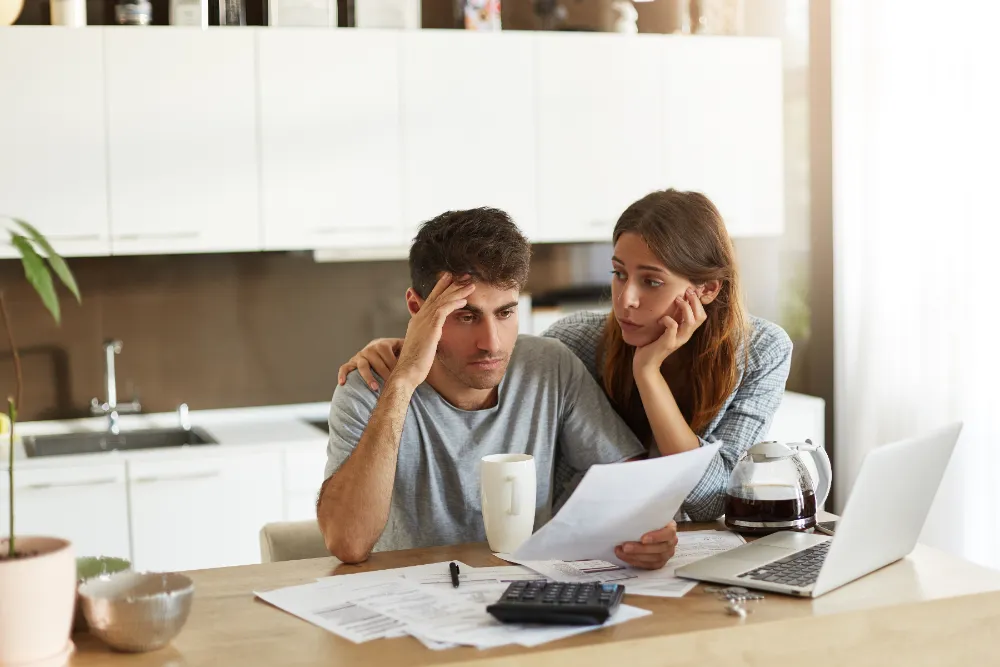 Couple reviewing financial documents together at home with laptop and calculator on table